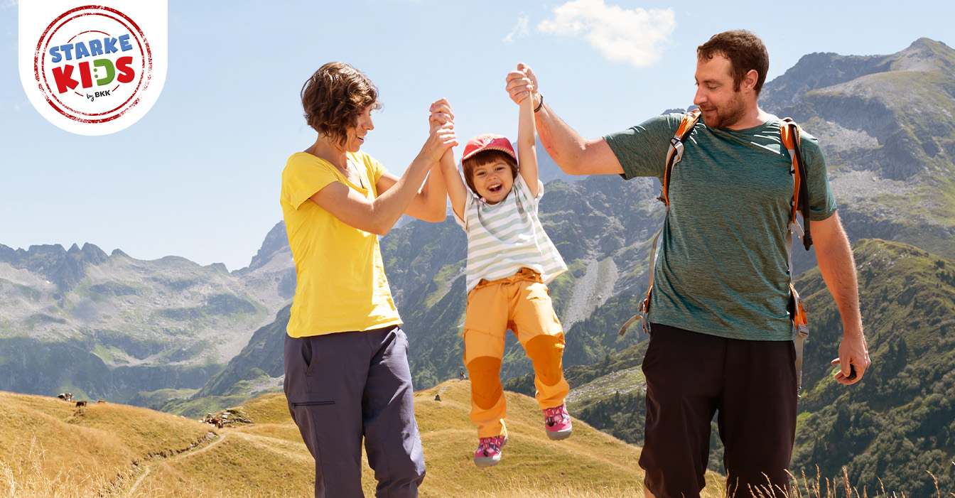 Zwei Erwachsene heben ein Kind an den Armen hoch. 