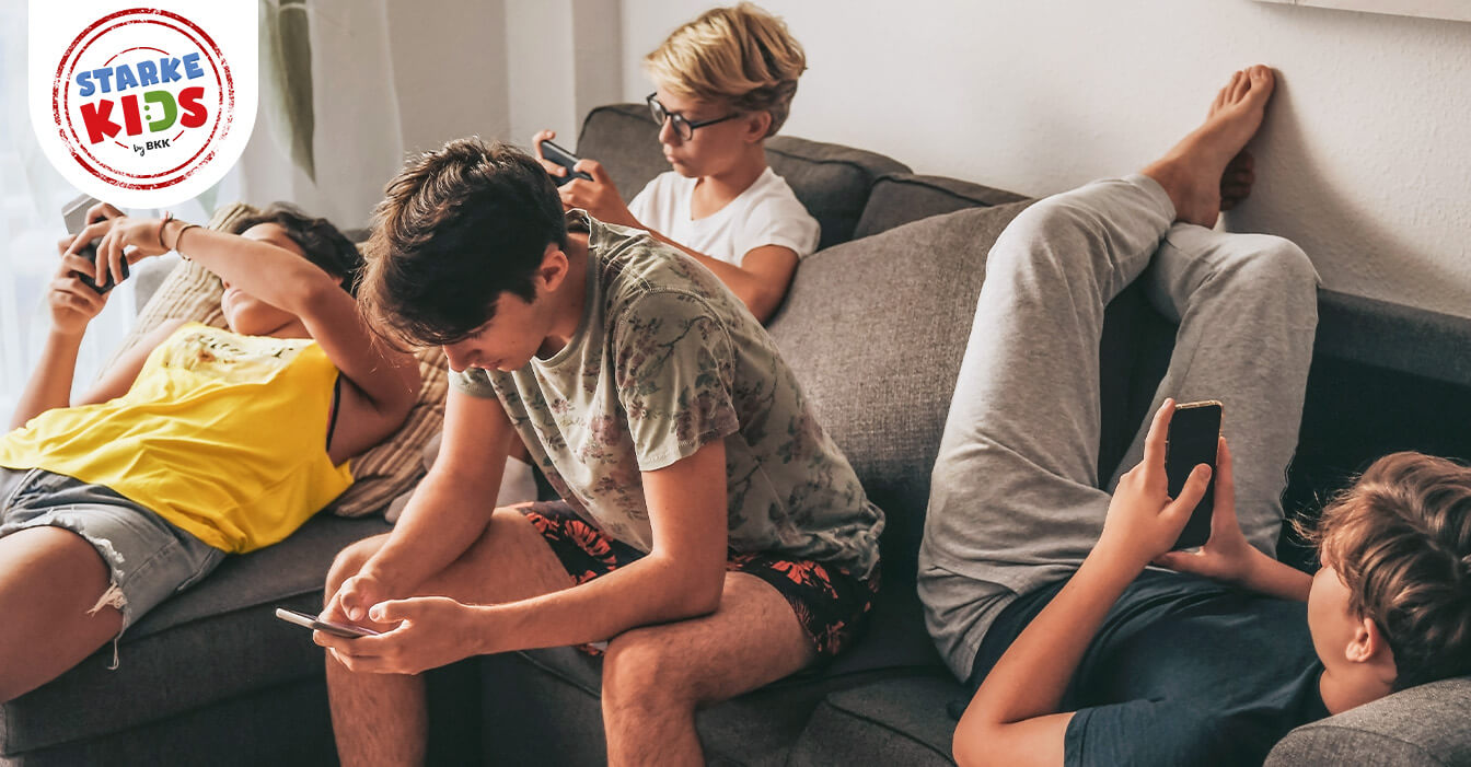 Eine Gruppe von Juggendlichen sitzt zusammen auf einem Sofa, jeder vertieft in sein eigenes Smartphone, ohne miteinander zu interagieren.